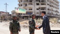 Presiden Suriah Bashar al-Assad berjabat tangan dengan seorang personel militer dalam kunjungannya ke situs militer di Darya awal Agustus.