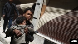 A Syrian boy carries a child while he runs for cover in the rebel-held area of Douma, east of the capital Damascus, as several air strikes pounded the city, April 22, 2015. 
