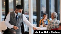 Seorang pelayan mengisi gelas di restoran seafood Mediterania Estiatorio Milos di Hudson Yards ketika restoran mulai membuka kembali layanan makan di dalam ruangan dengan kapasitas 25 persen di Manhattan, New York City, AS, 30 September 2020. (Foto: REUTE