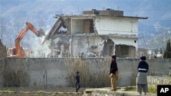 A police commando stands guard as authorities use heavy machinery to demolish Osama bin Laden's compound in Abbottabad, Pakistan, February 26, 2012.
