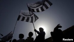 FILE - Supporters of the Jamaat-ud-Dawa Islamic organization are silhouetted against the sun as they raise flags while taking part in a rally in Lahore, May 25, 2012. 
