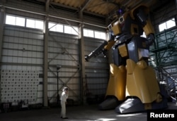 Sakakibara Kikai's engineer Go Sakakibara talks on a mobile phone to communicate with another engineer boarding the bipedal robot Mononofu during its demonstration at its factory in Shinto Village