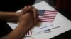 A participant fold her hands of a copy of the Oath of Allegiance while listening to speeches during a naturalization ceremony at historic Federal Hall, Friday, March 22, 2013 in New York.