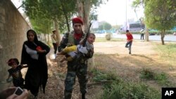 In this photo provided by Mehr News Agency, an Iranian army member carries a child from a shooting scene during a military parade marking the 38th anniversary of Iraq's 1980 invasion of Iran, in the southwestern city of Ahvaz, Iran, Sept. 22, 2018.