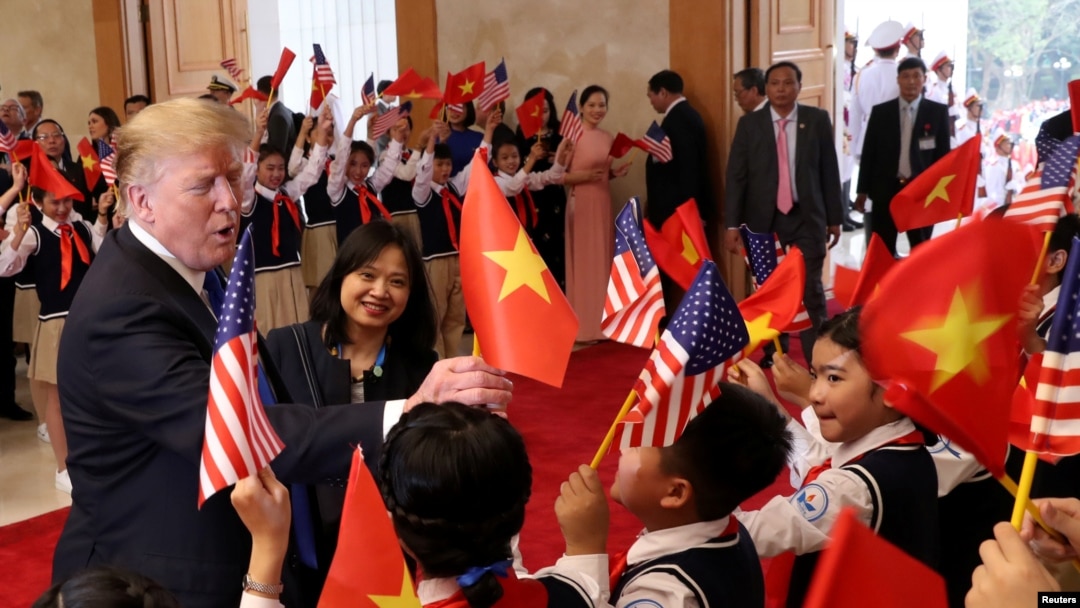 Presiden AS memegang bendera Vietnam saat disambut oleh para pelajar menjelang pertemuan dengan Perdana Menteri Vietnam Nguyen Xuan Phuc (tak tampak di foto) di Aula Pemerintah di Hanoi, Vietnam, 27 Februari 2019. 