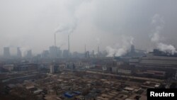 FILE - Smokestacks and cooling towers of a power plant rise above a low-rise neighborhood that borders a steel plant in Anyang, Henan province, China, Feb. 18, 2019.