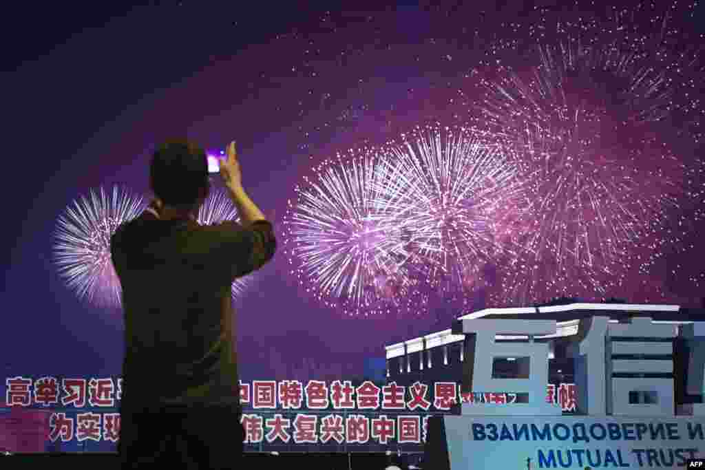 2018年6月9日，在山东青岛举行的上海合作组织（SCO）峰会期间，礼花绽放，焰火绚丽，一名男子用手机拍摄照片。此次上合组织青岛峰会在官媒渲染下盛况空前，中国为与会国代表举行了欢迎宴会，还有文艺演出和焰火表演。有一些推特用户以此和同一时段举行的工业7国峰会做比较，赞扬G7峰会之简朴，批评青岛峰会之奢华。有人说：&ldquo;西方富国开穷会，东方穷国开富会。&rdquo;