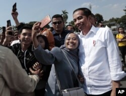 Seorang perempuan Muslim berfoto selfie dengan Presiden Indonesia Joko Widodo (kanan) saat berkunjung di Kota Tua, Jakarta, Jumat, 26 Juli 2019.