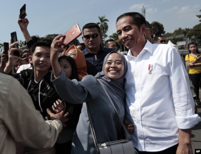 Seorang perempuan Muslim berfoto selfie dengan Presiden Indonesia Joko Widodo (kanan) saat berkunjung di Kota Tua, Jakarta, Jumat, 26 Juli 2019.