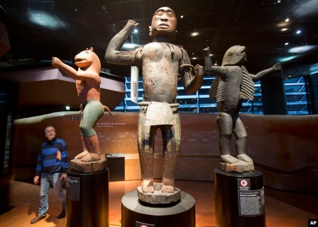 FILE - A visitor looks at wooden statues of the 19th century Dahomey Kingdom era, at the Quai Branly museum in Paris, France, Nov. 23, 2018. France is to return later this month artworks to Benin it took during the colonial era.