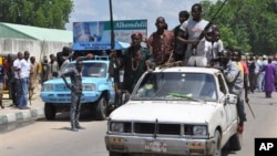 FILE - Vigilantes and local hunters armed with machetes and guns shout slogans as they gather outside the Emir's palace for a royal blessing to fight Islamist Militants in Maiduguri, Nigeria, Sept. 4, 2014. 