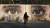 FILE - An Afghan woman waits for transportation in front of street art on a barrier wall of the NDS (National Directorate of Security) in Kabul, Afghanistan, Aug. 20, 2015. A group called the Art Lords created the eyes on the NDS wall as a warning to corrupt officials.