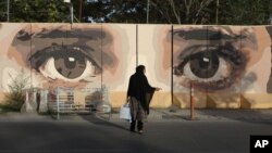 FILE - An Afghan woman waits for transportation in front of street art on a barrier wall of the NDS (National Directorate of Security) in Kabul, Afghanistan, Aug. 20, 2015. A group called the Art Lords created the eyes on the NDS wall as a warning to corrupt officials.