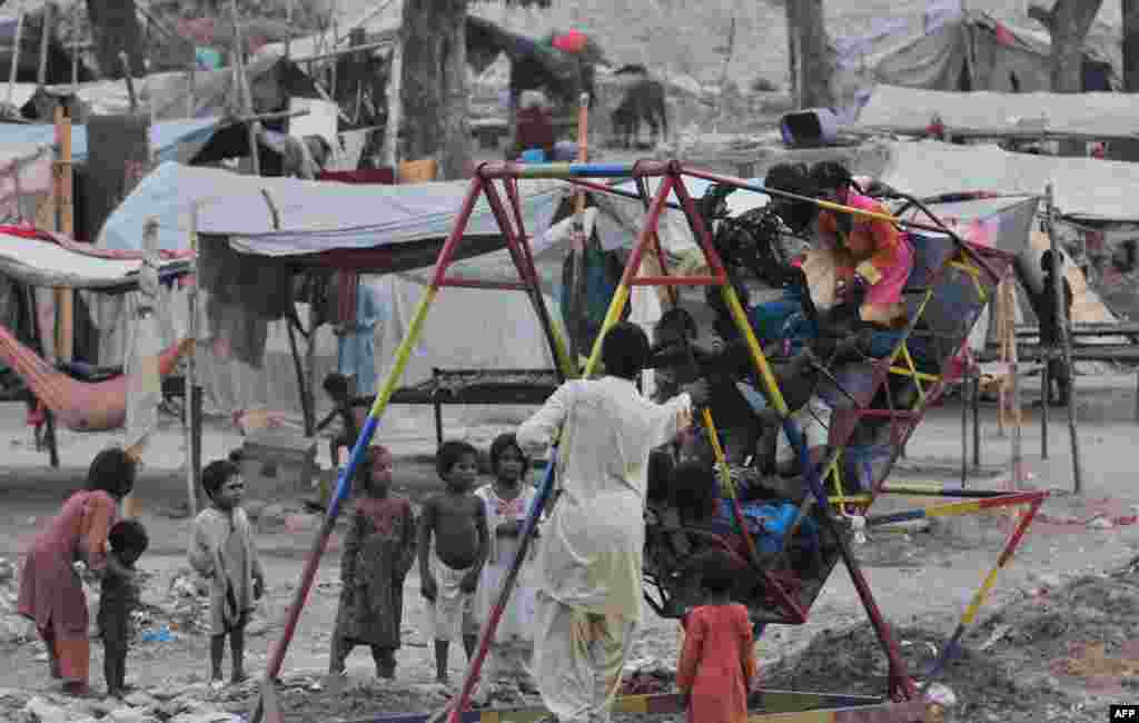 Anak-anak Pakistan bermain ayunan di dekat tenda-tenda darurat mereka di daerah kumuh kota Lahore.