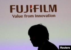 Siluet seorang pria tergambar di bawah logo Fujifilm Holdings saat berlangsungnya konferensi pers di Tokyo, Jepang, 31 Januari 2018. (REUTERS/Kim Kyung-Hoon)