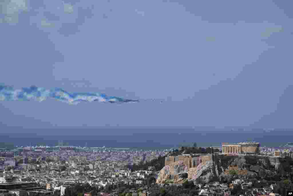 Alpha jets from the Patrouille de France team and two French Air Force Rafale jets spray lines of smoke in the colors of the Greek flag as they fly past the Parthenon Temple atop the Acropolis hill, Greece.