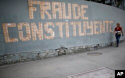 A pedestrian walks next to a message on a wall formed with Venezuelan currency that reads in Spanish: “The Constituent Assembly is a fraud” in Caracas, Venezuela, July 31, 2017.