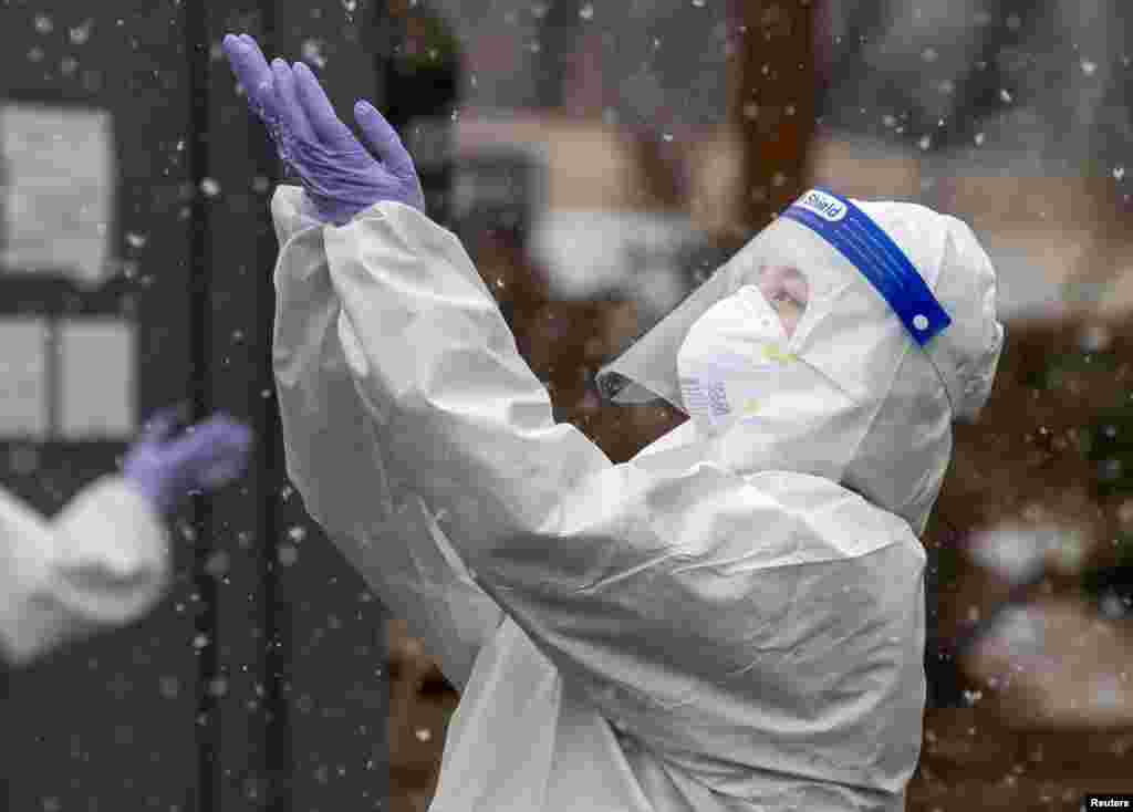 A health worker wearing protective clothing reaches for falling snow at a coronavirus testing site in Seoul, South Korea.