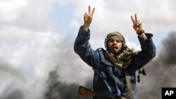 Borac iz pobunjeničkih postrojbi viče "Alah Akbar!" pred uništenim vozilima Gadafijeve vojske