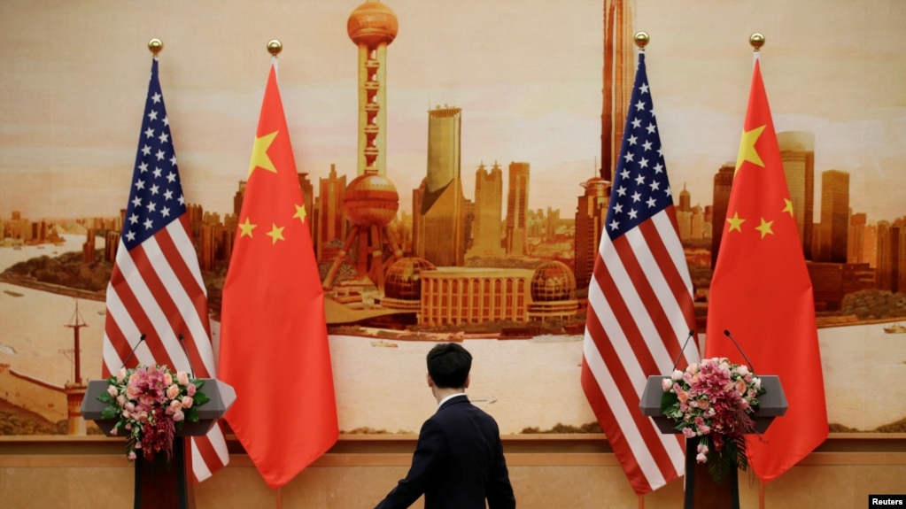 Un funcionario chino camina delante de las banderas de EE.UU. y China antes de la conferencia de prensa entre el secretario de Estado de EE.UU. Mike Pompeo y el canciller chino Wang Yi, en el Gran SalÃ³n del Pueblo, en Beijing, China, el 14 de junio de 2018.