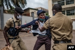 FILE - A demonstrator is arrested by Ugandan police officers at a protest for more food distribution by the government to people who have been struggling during the nationwide lockdown imposed to curb the spread of the COVID-19, in Kampala, May 18, 2020.