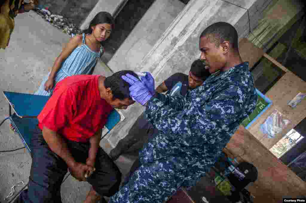 Hospital Corpsman Quinton Dotson, assigned to the U.S. Navy's forward-deployed aircraft carrier USS George Washington (CVN 73), from Rino, Nev., right, assists Philippine nurses in treating a patient's head wound at the Immaculate Conception School refug