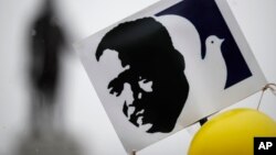 A placard bearing the likeness of slain civil rights leader Martin Luther King Jr. bobs above the crowd of marchers gathered beneath the statue of King, back, before the start of the annual parade to mark his birthday, Jan. 15, 2018, in Denver. 