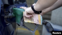 A worker pumps gas into a vehicle at a gas station belonging to Venezuela's state oil company PDVSA, as she holds bolivar notes, in Caracas, Feb. 13, 2016. Venezuela has the world's cheapest gasoline.