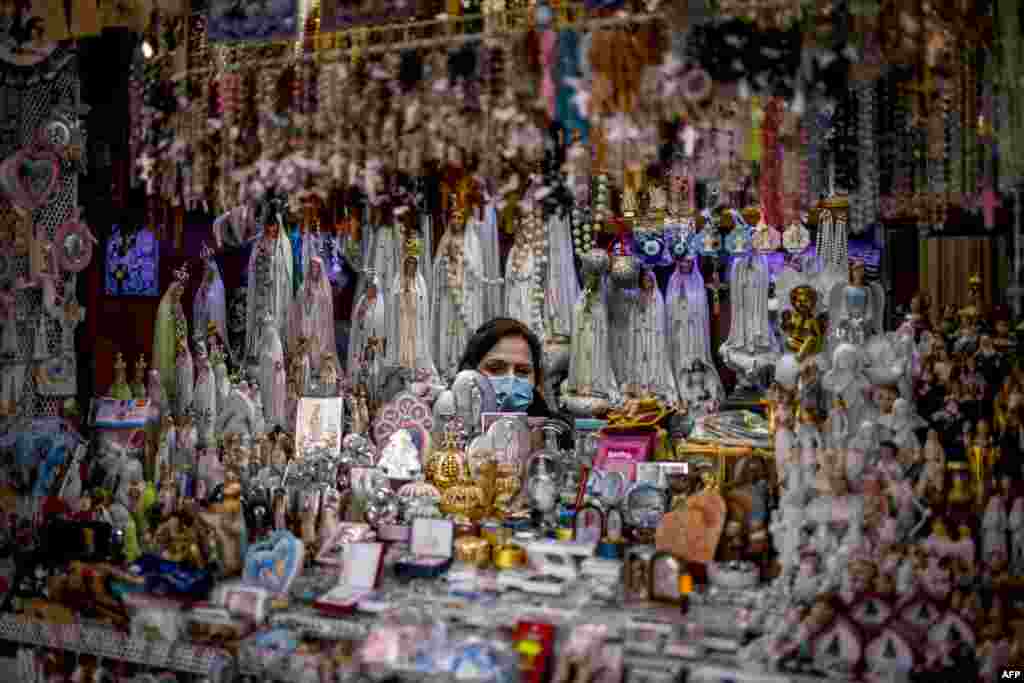 A seller of religious figurines waits for customers at her stall wearing a face mask during the 103rd anniversary of the apparitions of Our Lady of Fatima at the Fatima shrine in central Portuga.