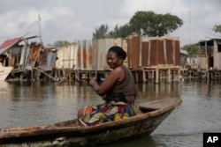FILE - A woman paddles a canoe past residents salvaging objects from houses demolished by government officials in Otodo-Gbame waterfront in Lagos, Nigeria, March.18, 2017.