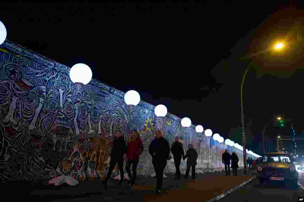 People pass by the art project 'Lichtgrenze 2014' (Border of Light) next to remaining parts of the Berlin Wall. The light installation featuring 8,000 luminous white balloons commemorates the division of Berlin, in the East Side Gallery in Berlin, Germany, Nov. 7, 2014.