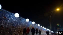 Ljudi prolaze pored osvetljenih balona - umetničkog projekta 'Lichtgrenze 2014'.