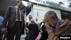 A bank manager explains the situation to pensioners waiting outside a branch of the National Bank of Greece hoping to get their pensions, in Thessaloniki, Greece.
