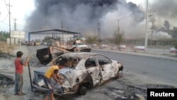 Anak-anak Irak berdiri dekat bangkai mobil yang terbakar dalam bentrokan antara pasukan keamanan dan militan Islamis terkait al-Qaida ISIL di Mosul, Irak utara (10/6).