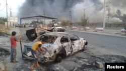 Civilian stand next to a burnt vehicle during clashes between Iraqi security forces and Islamic State in Iraq and the Levant (ISIL) in the northern Iraq city of Mosul, June 10, 2014. 