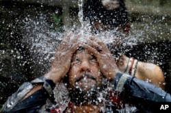 FILE - A Pakistani man cools himself off under a water supply to beat the heat during the holy fasting month of Ramadan, in Islamabad, Pakistan, June 7, 2016.
