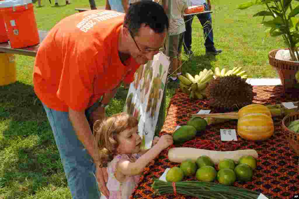 A man and his curious daughter at a display of tropical fruits and vegetables common in Cambodia.