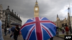 A pedestrian shelters from the rain beneath a Union Jack-themed umbrella near the Big Ben clock face and the Elizabeth Tower at the Houses of Parliament in central London, following the pro-Brexit result of the UK's EU referendum vote, June 25, 2016.