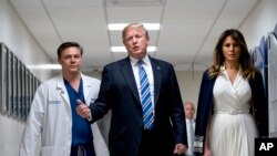 President Donald Trump, center, accompanied by first lady Melania Trump, right, and Dr. Igor Nichiporenko, left, speak to reporters while visiting with medical staff and victims of a mass shooting at a local school in Pompano Beach, Fla., Feb. 16, 2018.