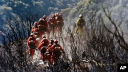 In this photo provided by the Santa Barbara County Fire Department, CAL FIRE Inmate Firefighting Hand Crew members hike through the charred landscape on their way to work east of Gibraltar Road above Montecito, Calif., Tuesday, Dec. 19, 2017. 