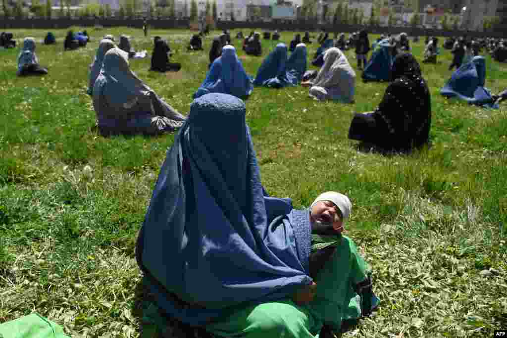 A woman wearing a burqa holds her child as she waits to receive free wheat from the government emergency committee during a government-imposed lockdown as a preventive measure against the coronavirus, in Kabul.