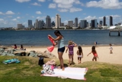 FILE - In this May 19, 2020, file photo, a family sets up at a beach looking out toward the San Diego skyline in Coronado, Calif.