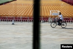 A man cycles past stands raised at Beijing's Tiananmen Square, Sept. 2, 2015, as the capital prepares for massive military parade.