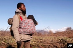 FILE - Jean-Paul Apetey of Ivory Coast helps carrying a baby near the village of Udovo, Macedonia, March 3, 2015.