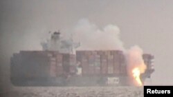 Fire cascades down from the deck of the container ship ZIM Kingston into the waters off the coast of Victoria, British Columbia, Canada, Oct. 23, 2021, as seen through a pair of binoculars, in this image obtained via social media.