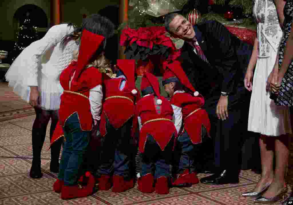 Tổng thống Mỹ Barack Obama vui cười bên cạnh những em nhỏ ăn mặc như nhân vật thần thoại elf tụ tập quanh một cây thông Giáng sinh xem quà của mình, do gia đình Tổng thống tặng, tại Bảo tàng Kiến trúc Quốc gia ở thủ đô Washington, ngày 15 tháng 12, 2013. 