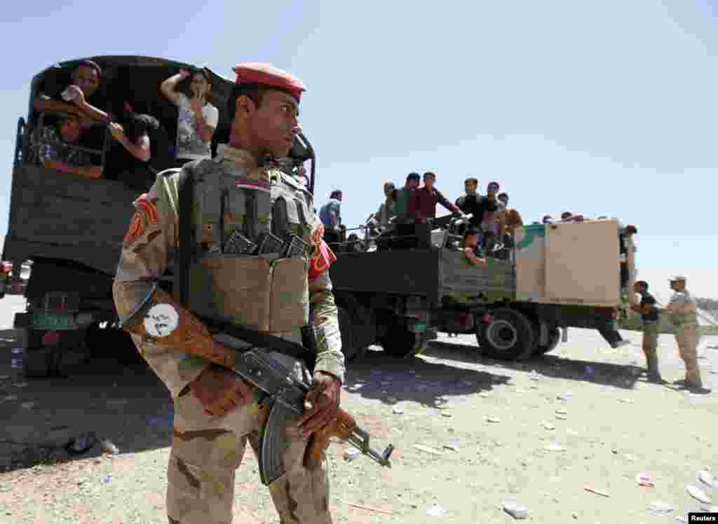 A member of Iraqi security forces stands guard in front of volunteers who joined the army to fight the Islamic State of Iraq and the Levant, Baghdad, June 17, 2014.