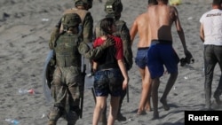 FILE - A female migrant is led by a Spanish female soldier as she is deported to Morocco after she crossed the border swimming from Morocco to Spain, at El Tarajal beach, in Ceuta, Spain, May 19, 2021. 