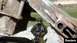 FILE - An Israeli soldier stands guard during the demolition of a Palestinian house at the order of the Israeli army, in the West Bank town of Dura, south of Hebron January 20, 2016. 