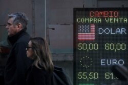 Pedestrians walk past an electronic board showing currency exchange rates in Buenos Aires' financial district, Argentina, Aug. 12, 2019.